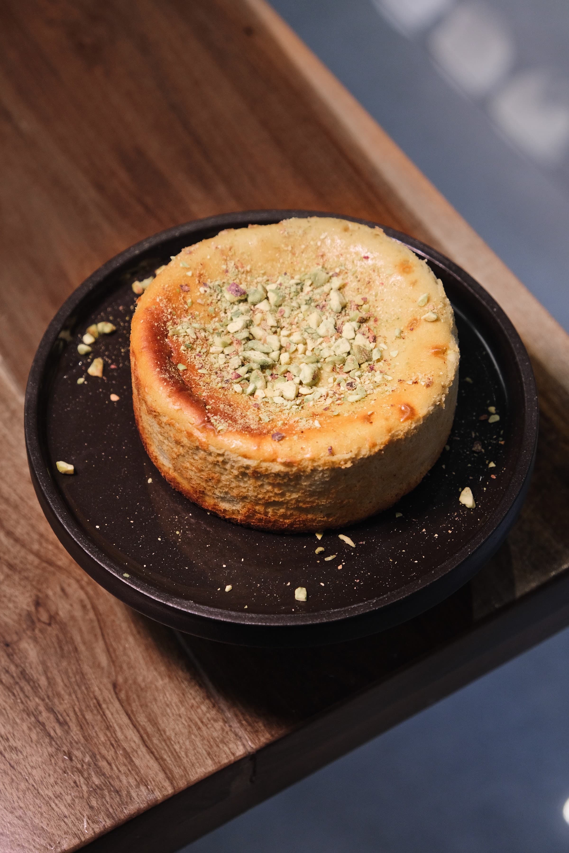 Tarta vasca de pistacho recién horneada, con pistacho picado por encima, sobre un plato oscuro